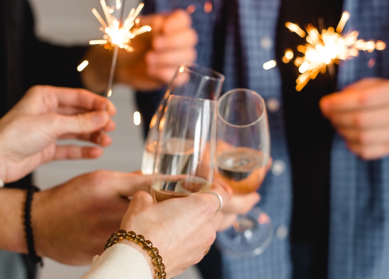 champagne glasses in friends hands with sparklers indoor holiday time