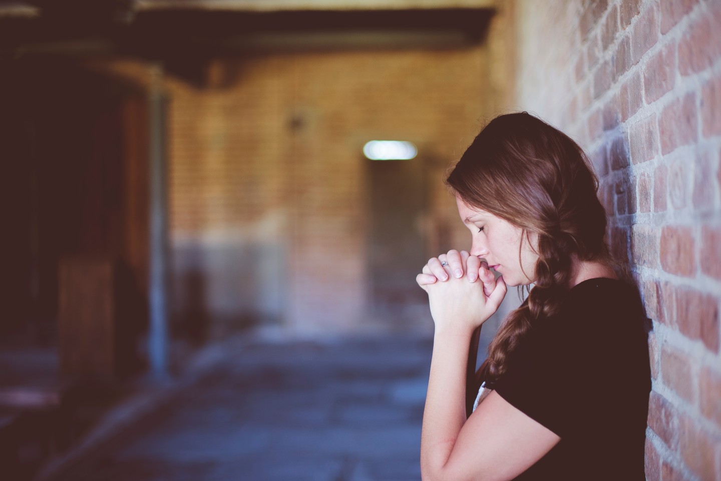 woman hands in front of head bowing down brick wall