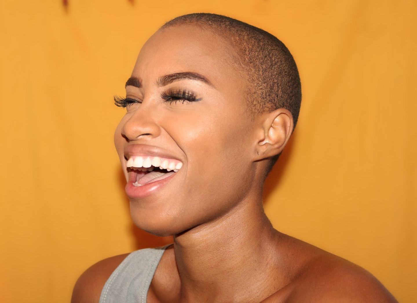 woman shaved head long eyelashes yellow background smile