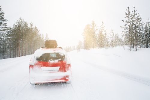 Red car with a packed roof rack driving down a snowy road