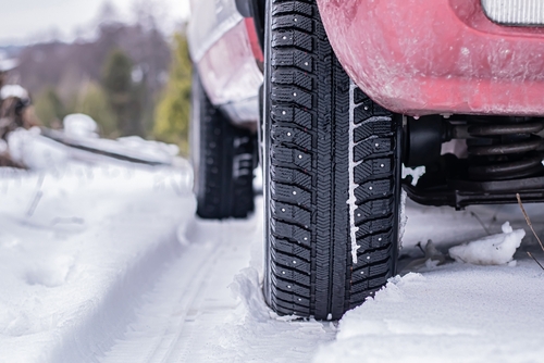 Red vehicle driving in snow with studded winter tires