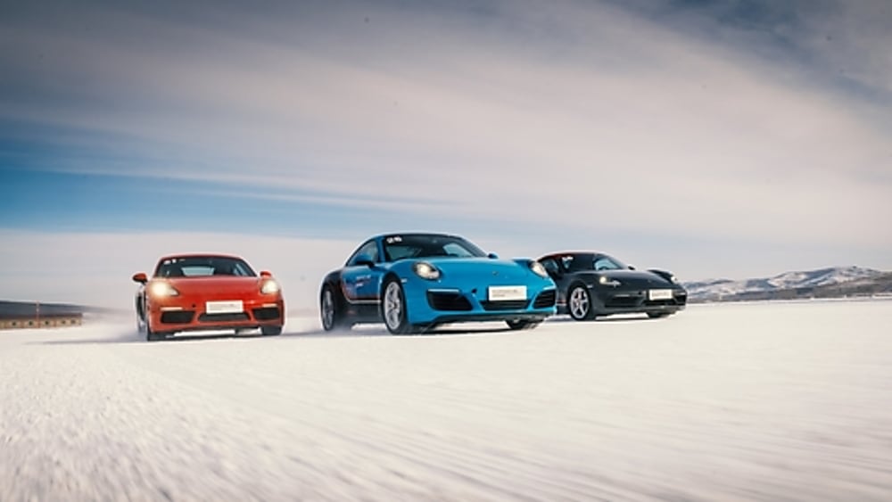 Three Porsche 911 sports cars driving on a snow field