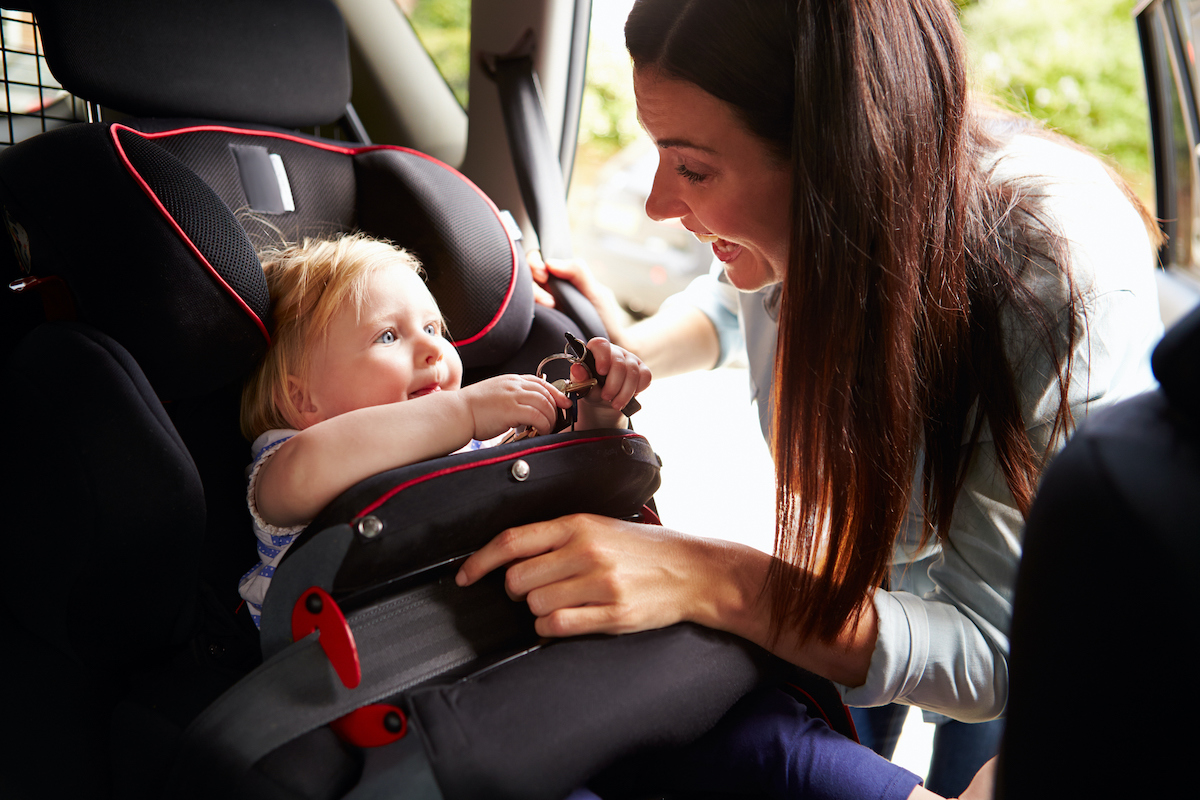 Mum strapping child in with car seat safety shield
