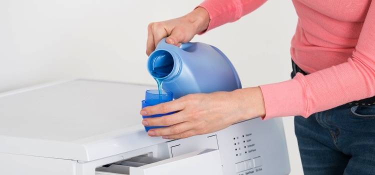 kvinde hælder flydende vaskemiddel i vaskemaskine