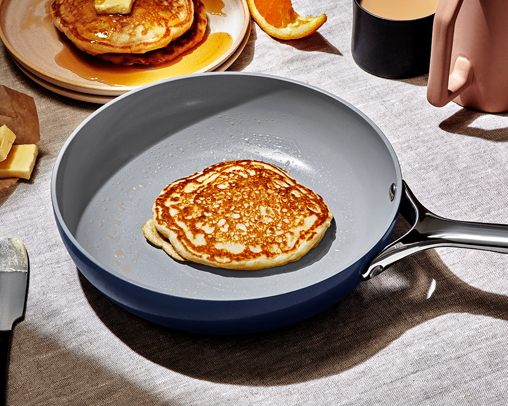 pancake in a sauté pan ready to be flipped with wooden kitchen utensils