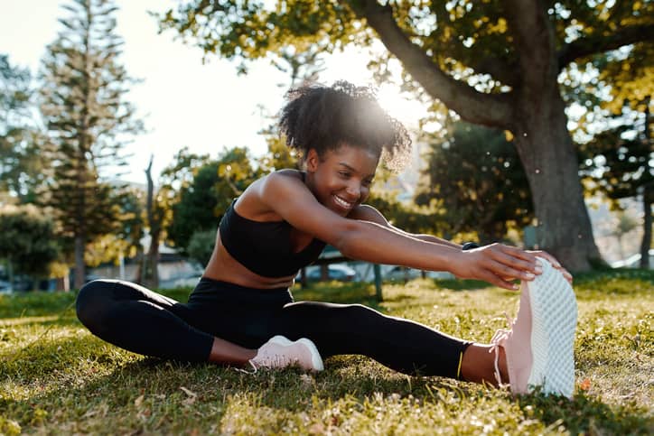 Woman stretching her legs on the lawn after running. Regular exercise can help get rid of trapped wind or IBS, which both cause pain in the lower right abdomen.