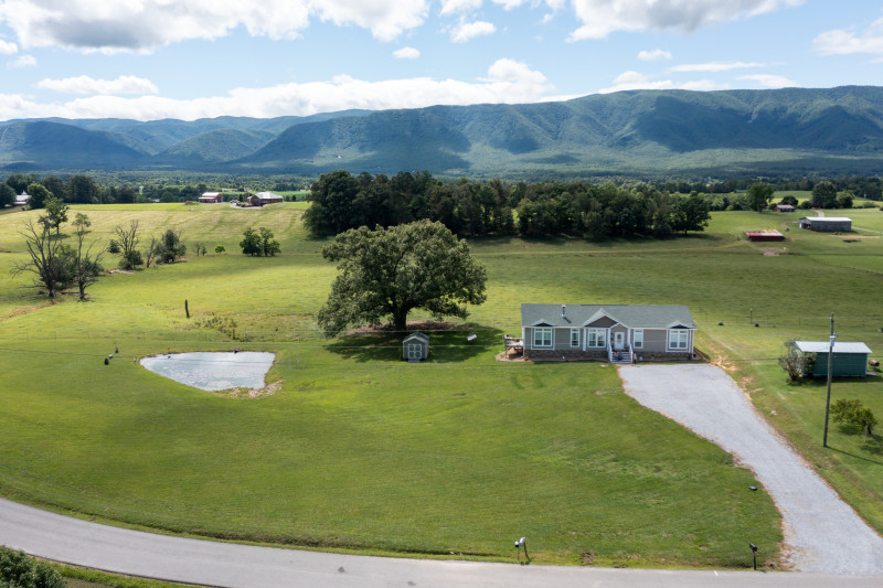 Tan manufactured home nestled into East Tennessee landscape with lush green grass, a pond and mountains in the background.